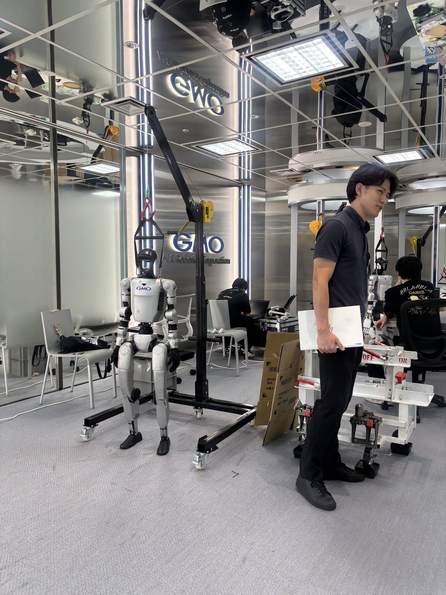 吊り下げ架台の人型の機体と、その横に立つスタッフ